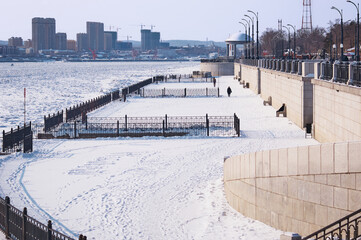 Snow-covered city embankment of the Amur River in winter. The lower level with the townspeople...