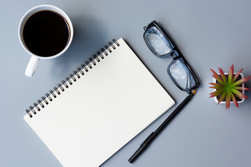 Notepad with cup of coffee and reading glasses on a desk. Directly above.