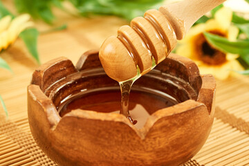 Liquid fresh honey drips from a dipper into a wooden bowl