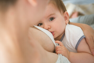 Young caucasian mom with infante in interior location. Mom nursing baby in a white bedroom. Nursery...