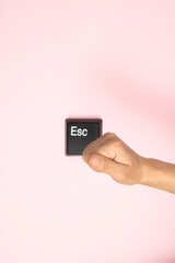 Hand prepares to hit the Esc button on pink background. Escape from dept, love, bad situation, relationship etc. Flat lay.