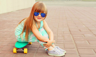 Portrait of stylish little girl child with skateboard on city street