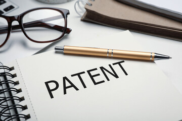 Notebook with word PATENT and pen on table, closeup