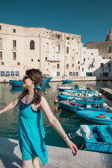 Fototapeta na wymiar Woman with a blue dress in the picturesque marina of Monopoli, a a little village in south Italy in summer