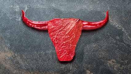 T-bone beef steak and hot peppers arranged in a shape of bull head. Conceptual food picture.