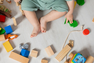 Obraz na płótnie Canvas closeup of the bare feet of baby in green bodysuit playing on the floor with wooden educational toys. products for children, early development, nursery kindergarten. space for text. High quality photo