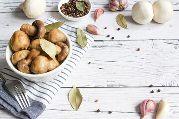 Champignons marinated, pickled mushrooms with spice in bowl on the wooden background. Marinated mushrooms with garlic, black pepper and bay leaf. 