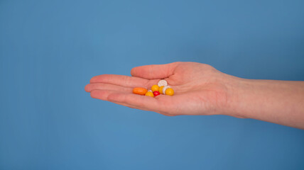 Tablets in hand. Outstretched hand with vitamins. The medicine. Hand with pills on a blue background.