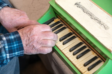 An elderly man plays a toy piano. Hands press the keys of an old children's instrument.