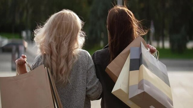 Shopping Together. Season Sale. Shopaholic Lifestyle. Back View Of Stylish Women Friends Walking On Sunny City Street With Store Bags.