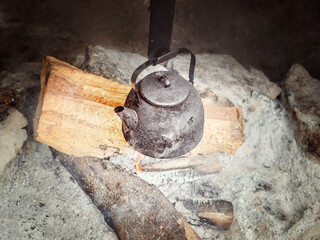 A charred metal kettle is boiled over burning wood and coals. Tea drinking in field conditions
