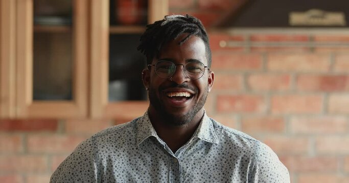 Headshot portrait of handsome bearded young African American male hipster looking at camera with sincere candid laughter. Joyful emotional young guy laughing having fun enjoying good day funny news