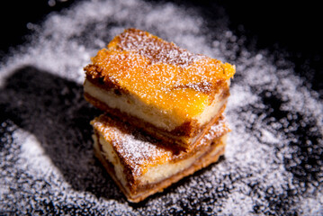 Besquit, cake on a black background, sprinkled with powdered sugar, dark and light layer of beckett on a black background, copy space