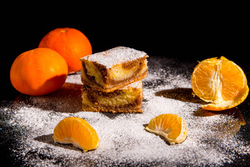 Besquit, cake on a black background, sprinkled with icing sugar with mandorin, dark and light layer of beckett on a black background, copy space