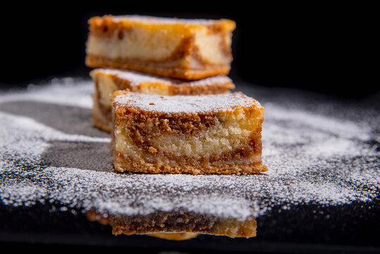 Besquit, cake on a black background, sprinkled with powdered sugar, dark and light layer of beckett on a black background, copy space