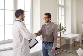 Friendly young male doctor shakes hands and greets patient in modern medical clinic. Young...