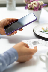 A woman scans a QR code using a phone in a cafe.