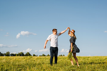 Happy laughing love couple dancing together in field on horizon on sunny day outdoors. Young caucasian heterosexual family romantic trip or walk in nature. Relationship, love concept