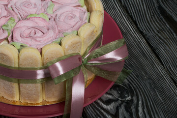 Cake with Savoiardi cookies and marshmallow roses. Tied with ribbon. The ribbon is tied into a bow.