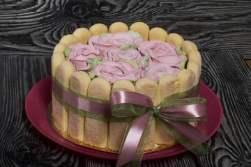 Cake with Savoiardi cookies and marshmallow roses. Tied with ribbon. The ribbon is tied into a bow.