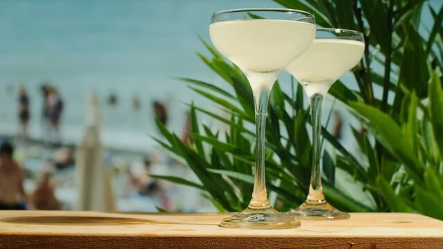 Beach bar. Cocktails on table bar, sea on background. Two drinking glasses of daiquiri cocktails decorated fresh flowers. Summer sea resort concept.