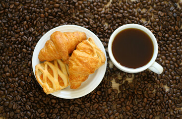 coffee mug and croissants on a background of coffee beans on a wooden table