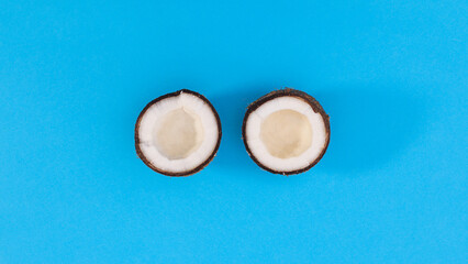 Obraz na płótnie Canvas Two parts of sliced tropic coconut onbright cyan background. Flat lay exotic food