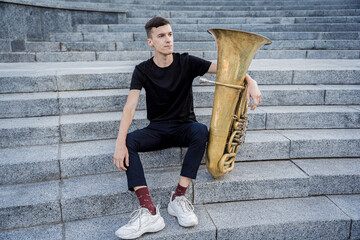 Young street musician playing tuba sitting on granite steps