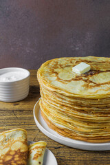 A high stack of pancakes with a piece of butter on a wooden background. Maslenitsa
