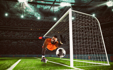 Goalkeeper in orange uniform catches the ball in the stadium during a football game