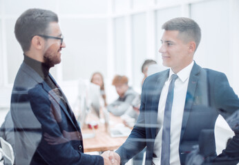 Fototapeta premium through the glass. business partners handshake in the office