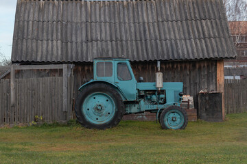 Green tractor on a grass in front of a wooden shed and a fence by autumn day