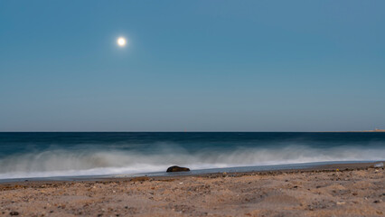 Overnight on the Red Sea beach. The full moon is shining in the blue sky. Turquoise waves foam on...