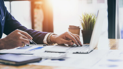 Closeup hands of businessman using laptop and holding pen analysis financial charts audit data.