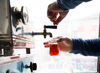pouring tea from a big teapot into a teacup. steel chai boiler for public spaces.