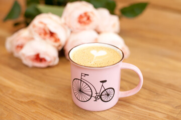 Cappuccino cup of coffee with heart latte art and pink roses on wooden table - Valentines Day card. 
 Valentines day surprise - cup of coffee with heart latte art and roses flowers background.
