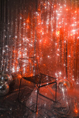 Black metal chair and silver disco ball on a glittery red background. Christmas sparkling star lights, party mood