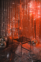 Black metal chair and silver disco ball on a glittery red background. Christmas sparkling lights, party mood