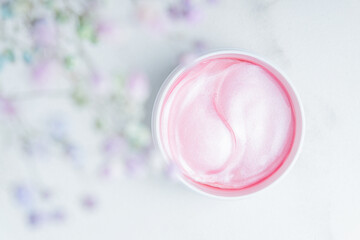 Pink patches on a marblel background next to pastel flowers. Natural flower extract cosmetics, beauty and fashion. Patches for moisturizing in a jar, flat lay, top view.