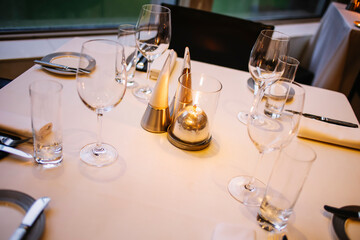 Beautifully set dinner table in a restaurant. Romantic fine dining table with cutleries, plates, wine glasses, napkins and naperies on the table.
