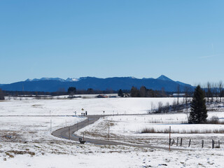 Die Stra&szlig;e vom Kloster Reutberg zum Kirchsee mit idyllischen Moorlandschaft, sch&ouml;ner Aussicht zwischen die schneebedeckten H&uuml;gel schneebedeckten und die Gipfel der oberbayerischen Alpen 