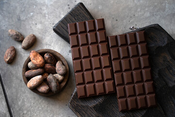 Stack of chocolate bars with cocoa beans. Flat lay composition with delicious chocolate on black background. Space for text