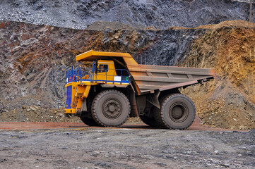 Extraction of iron ore. A mining dump truck transports iron ore along a side carrea. Special equipment works in a quarry