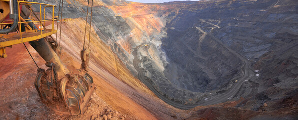 excavator bucket lies on the edge of the side of the iron ore quarry. Quarry panorama