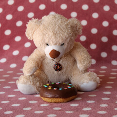 Teddy bear sitting in front of chocolate frosted donut