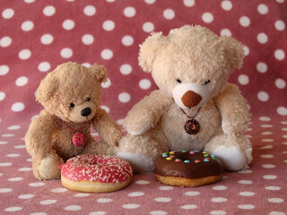 Two teddy bears sitting in front of frosted donuts