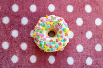 donut with white frosting and colorful confetti on spotted pink background