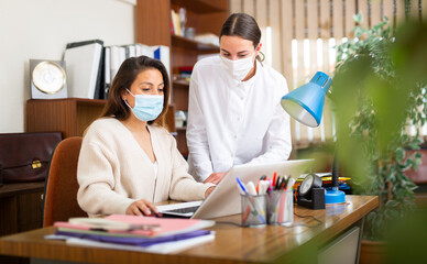 Portrait of two business woman in protective face masks chatting about work in office