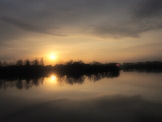 Lifting sun over the water. River bank and horizon. Bright clouds are painted by the evening sun....