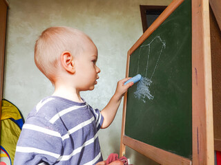 boy drawing with blue chalk on a green board